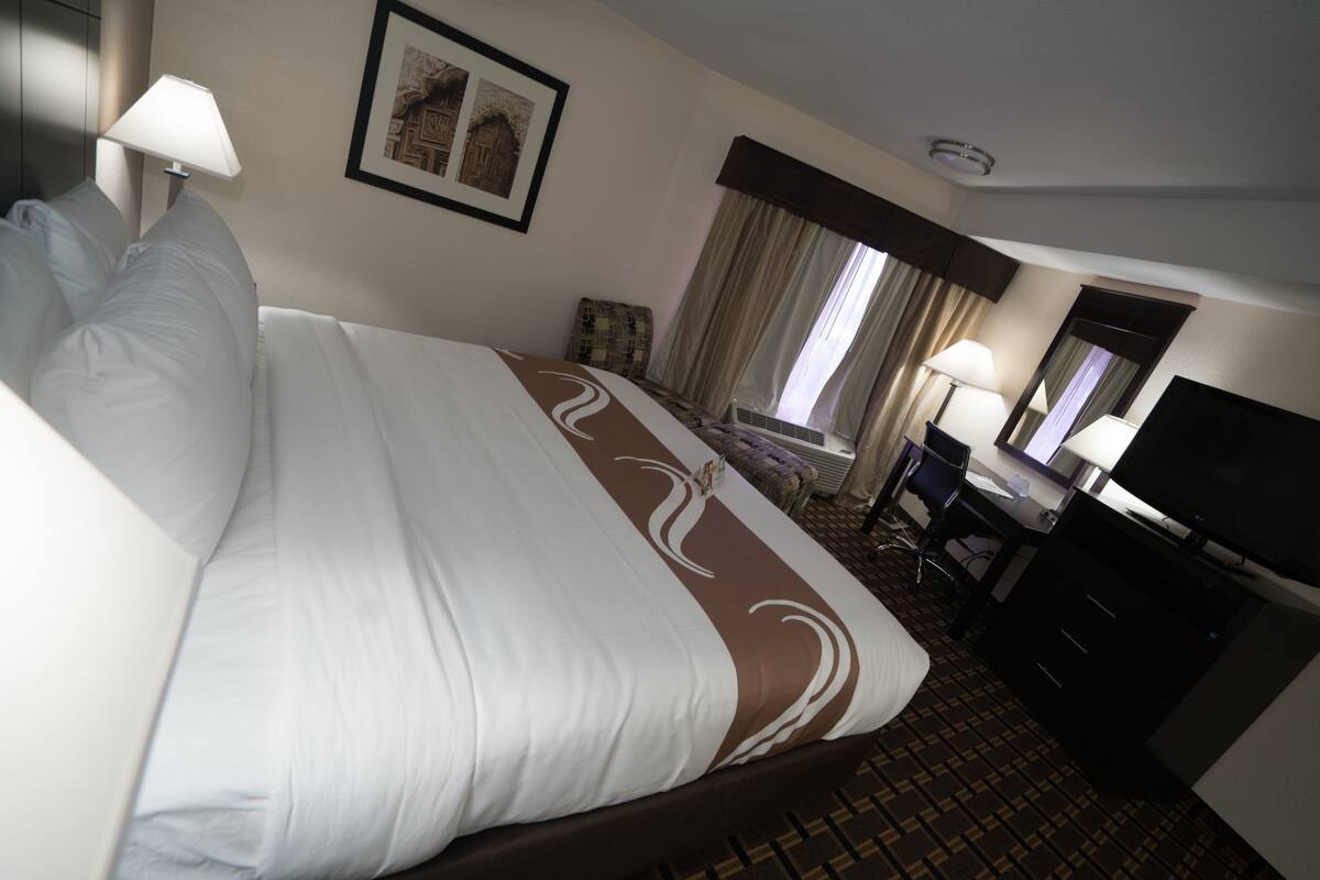 A hotel room with a large bed, a desk, a chair, a television, and a window with curtains.