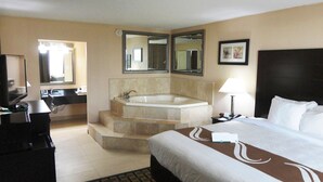 A hotel room with a large bed, a separate bathroom with a bathtub, a desk with a computer, and a TV.