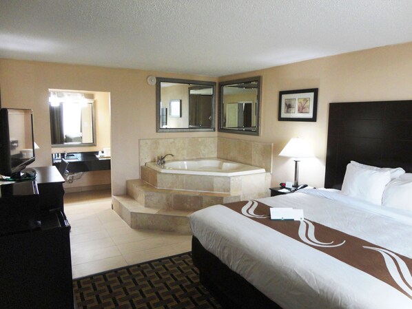A hotel room with a large bed, a separate bathroom with a bathtub, a desk with a computer, and a TV.
