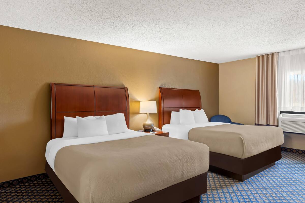 Quarto de hotel com duas camas, uma mesa de cabeceira com luminária e um ar condicionado.