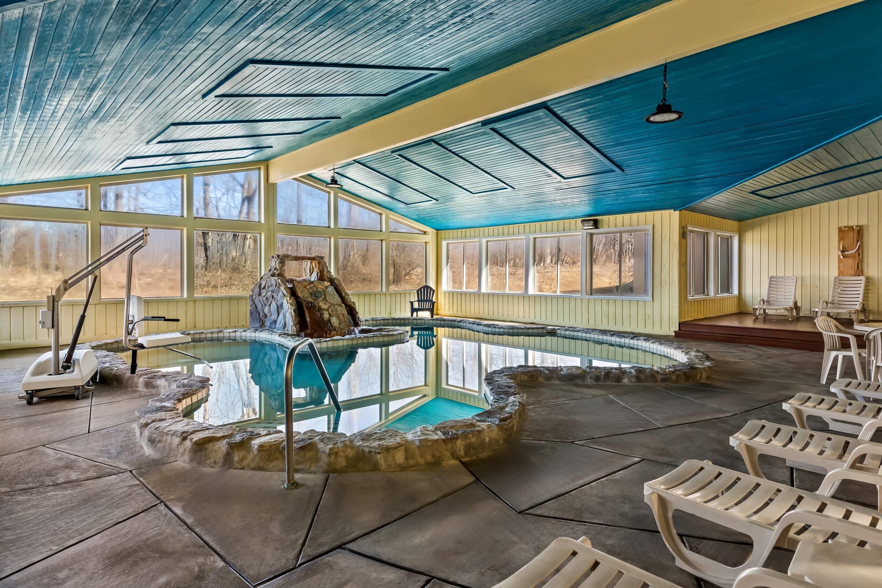An indoor swimming pool with stone steps, a lifeguard chair, and lounge chairs.