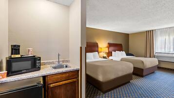 Une chambre d’hôtel avec une kitchenette, deux lits, une salle de bain et une fenêtre avec des rideaux.