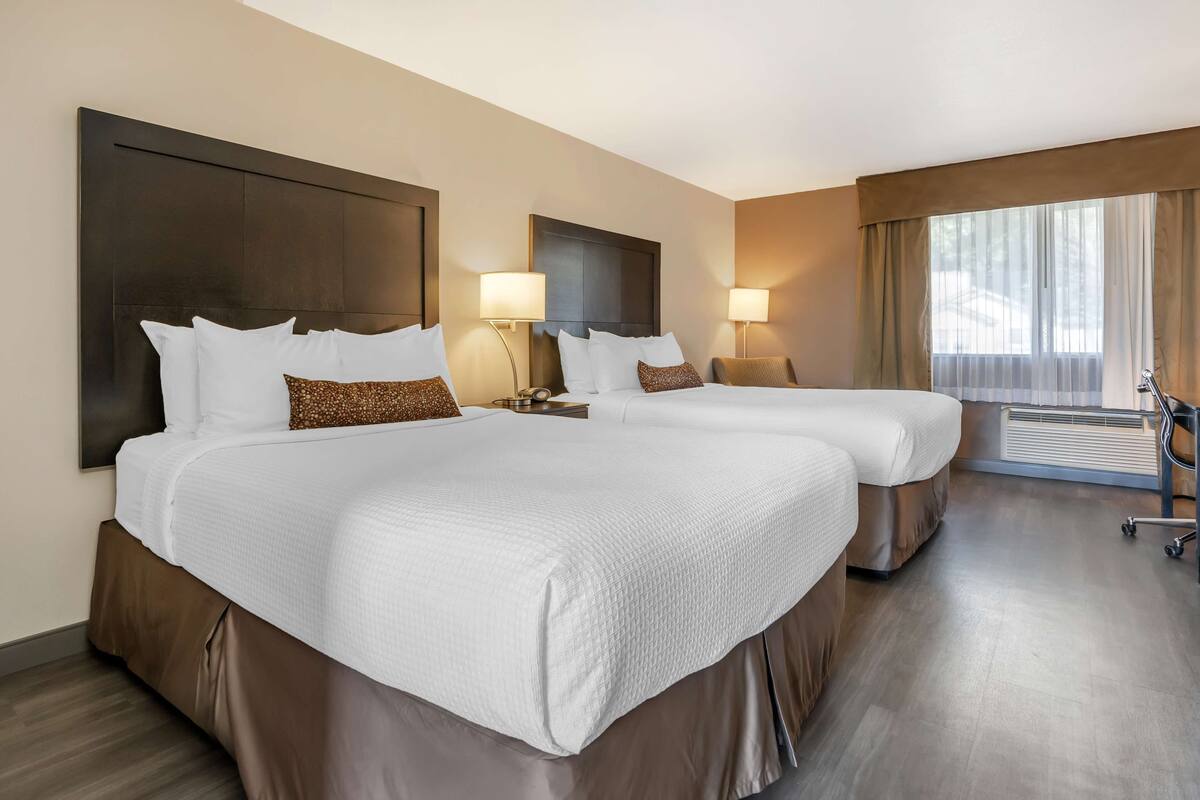 A hotel room with two beds, a large window with curtains, a desk, and a chair.