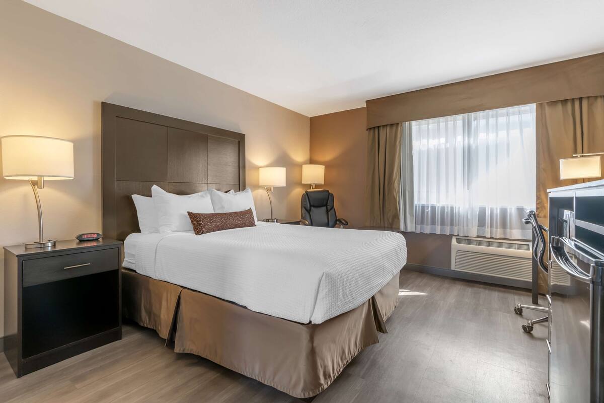 A hotel room with a large bed, bedside lamps, a desk, and a chair.