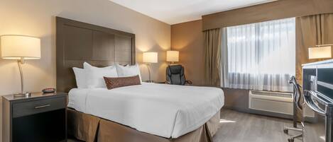 A hotel room with a large bed, bedside lamps, a desk, and a chair.