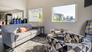 A modern living room with a grey sofa, patterned armchair, and a coffee table. Large windows provide natural light and a view of the outside. - Best Western Inn Of Vancouver (Vancouver)