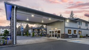 A hotel with a covered entrance, a sign indicating a 12'6" clearance, and a parking lot with a few vehicles. - Best Western Inn Of Vancouver (Vancouver)