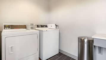 A laundry room with two white washing machines, a stainless steel trash can, and a white countertop.