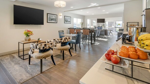 A spacious living area with a dining table, chairs, and a buffet table with fruits. - Best Western Inn Of Vancouver (Vancouver)