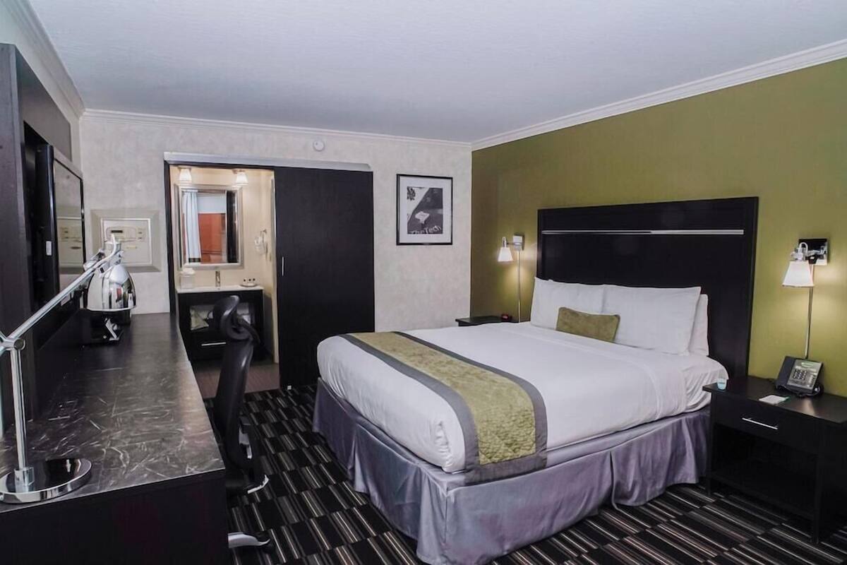 Ein Hotelzimmer mit Bett, Schreibtisch, Stuhl, Spiegel, Nachttisch und Lampe.