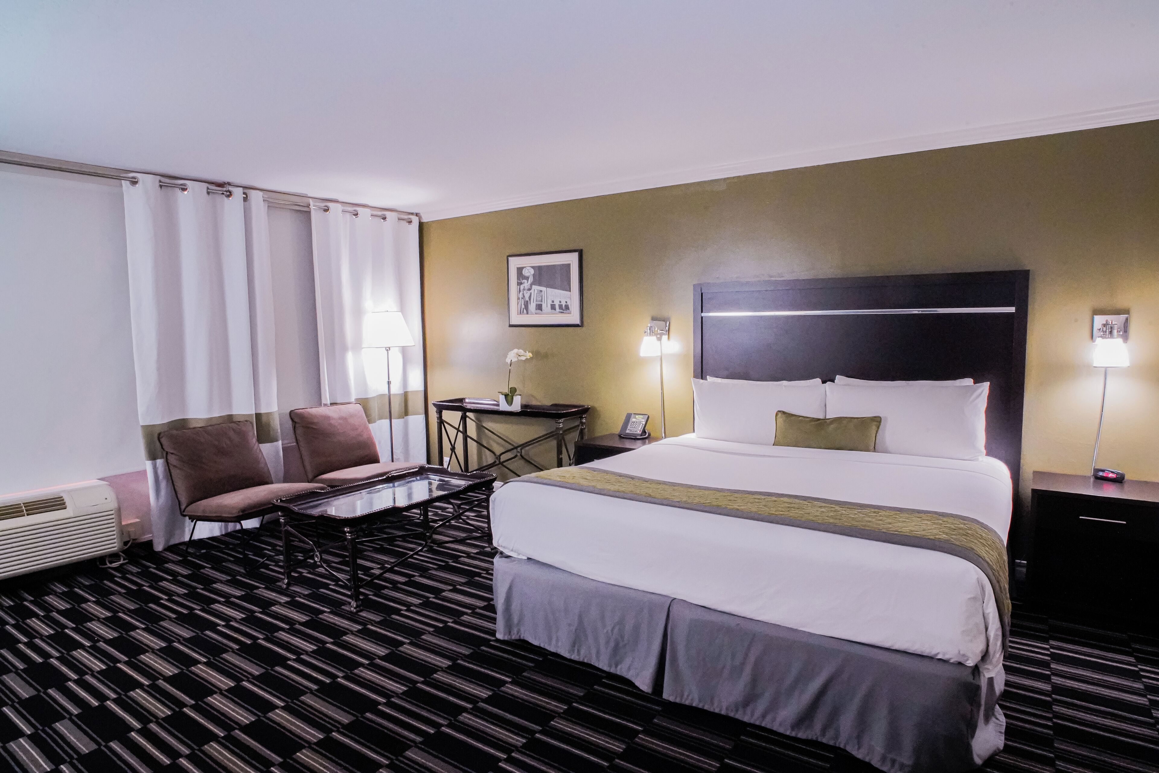 Habitación de hotel con una cama grande, dos sillas, una mesita pequeña y un escritorio con lámpara.