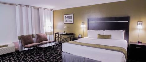 Habitación de hotel con una cama grande, dos sillas, una mesita pequeña y un escritorio con lámpara.