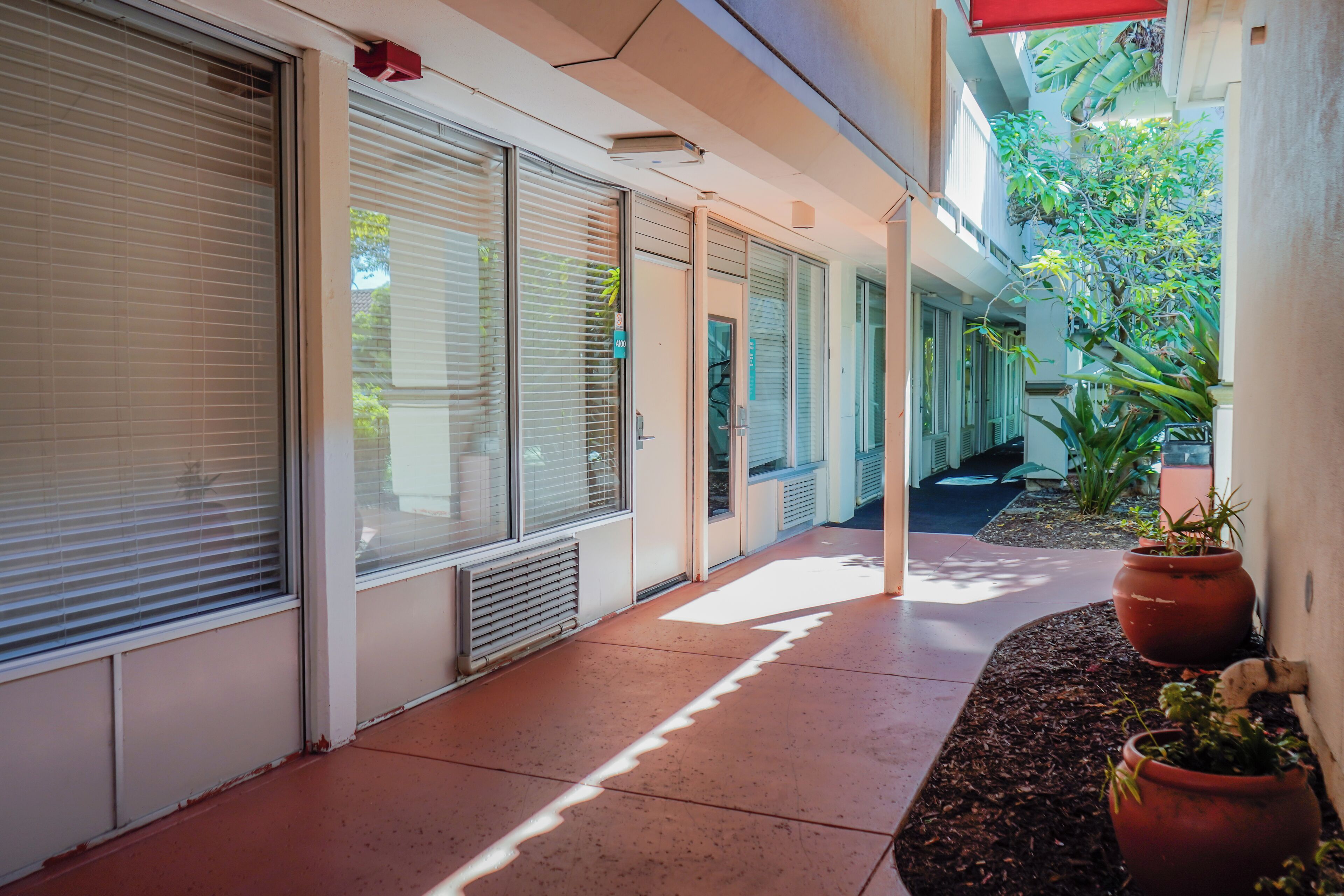 A covered outdoor corridor with closed sliding glass doors, potted plants, and a concrete floor.