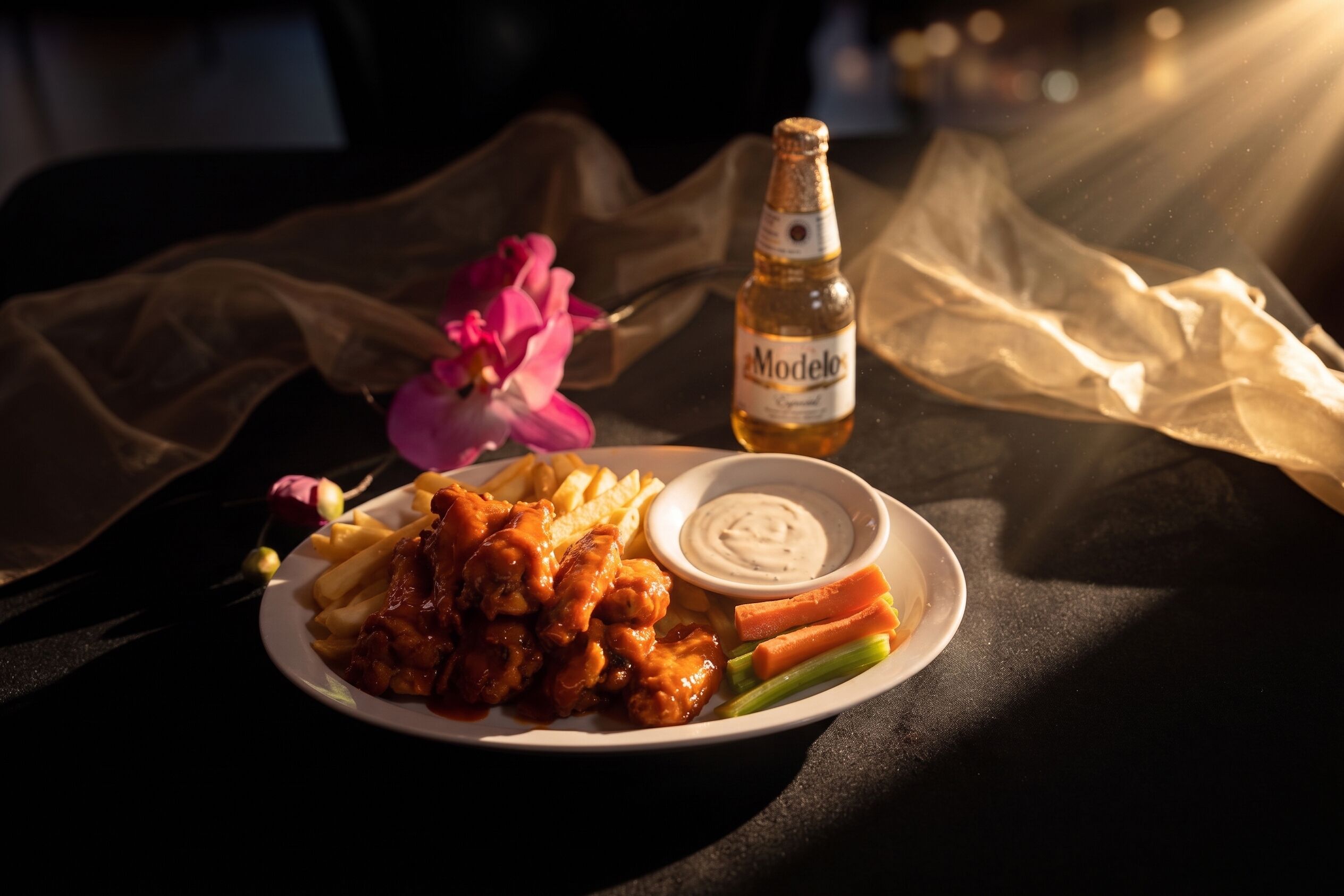 A plate of food with a bottle of Modelo beer, a bowl of sauce, and a flower on a table.
