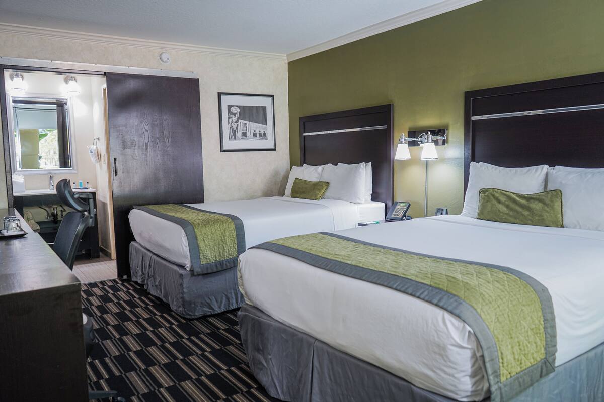 Ein Hotelzimmer mit zwei Betten, einem Schreibtisch, einem Stuhl, einem Spiegel und einem gerahmten Bild an der Wand.