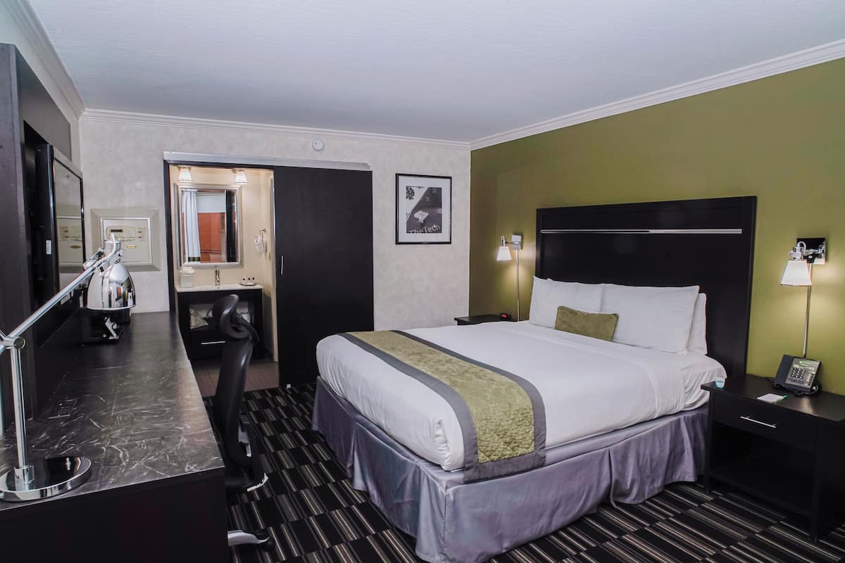 Ein Hotelzimmer mit Bett, Nachttisch, Lampe und Schreibtisch mit Stuhl.