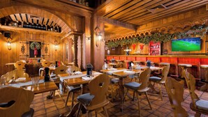 Un restaurante con interiores de madera, mesas, sillas, una zona de bar y una pantalla de televisión mostrando un evento deportivo.