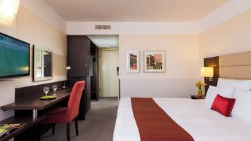 Habitación de hotel con cama, escritorio con silla, televisor y cuadros en la pared.