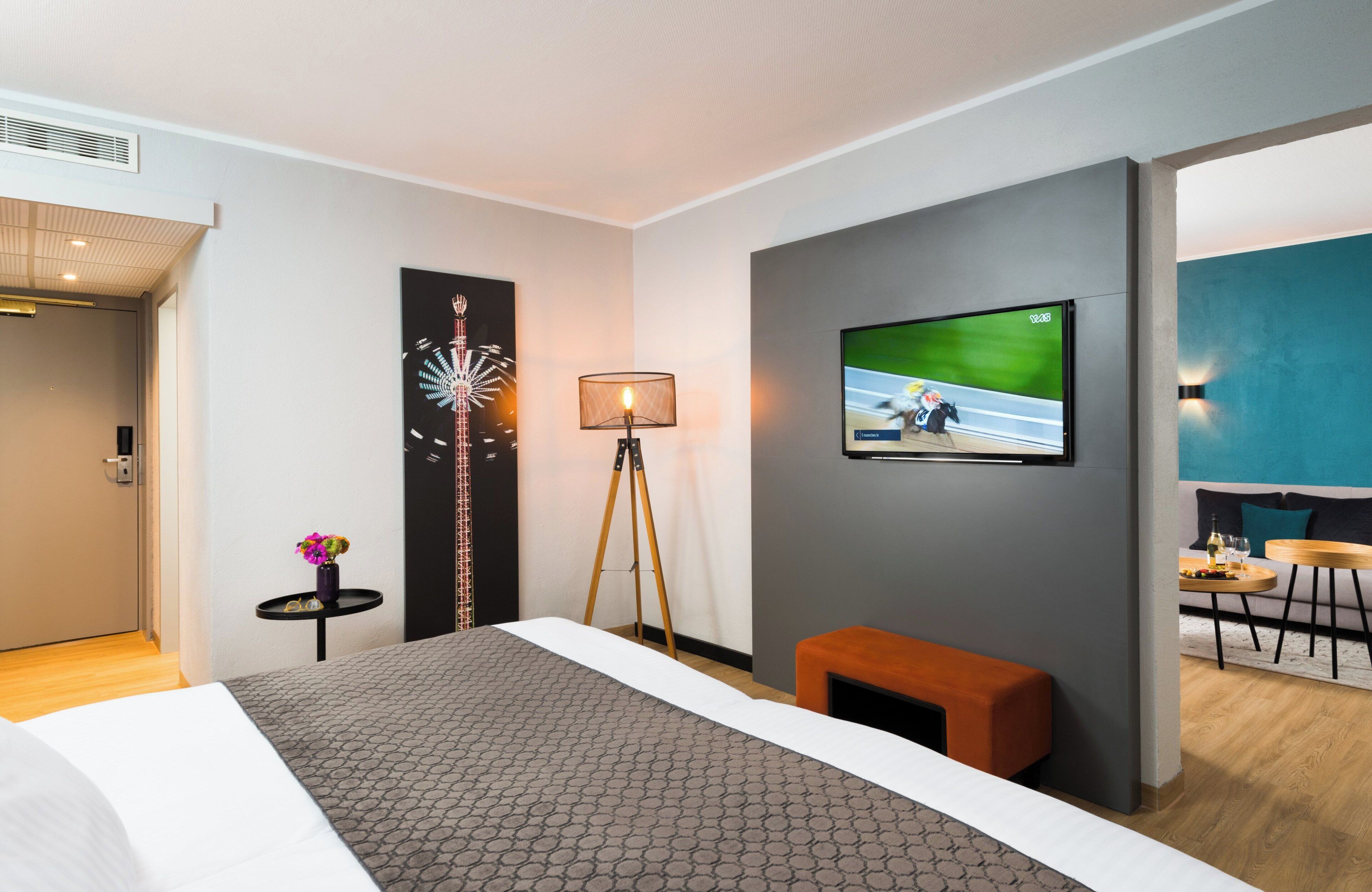 Una habitación de hotel moderna con una cama, un televisor en la pared, una mesita con una lámpara y un banco.