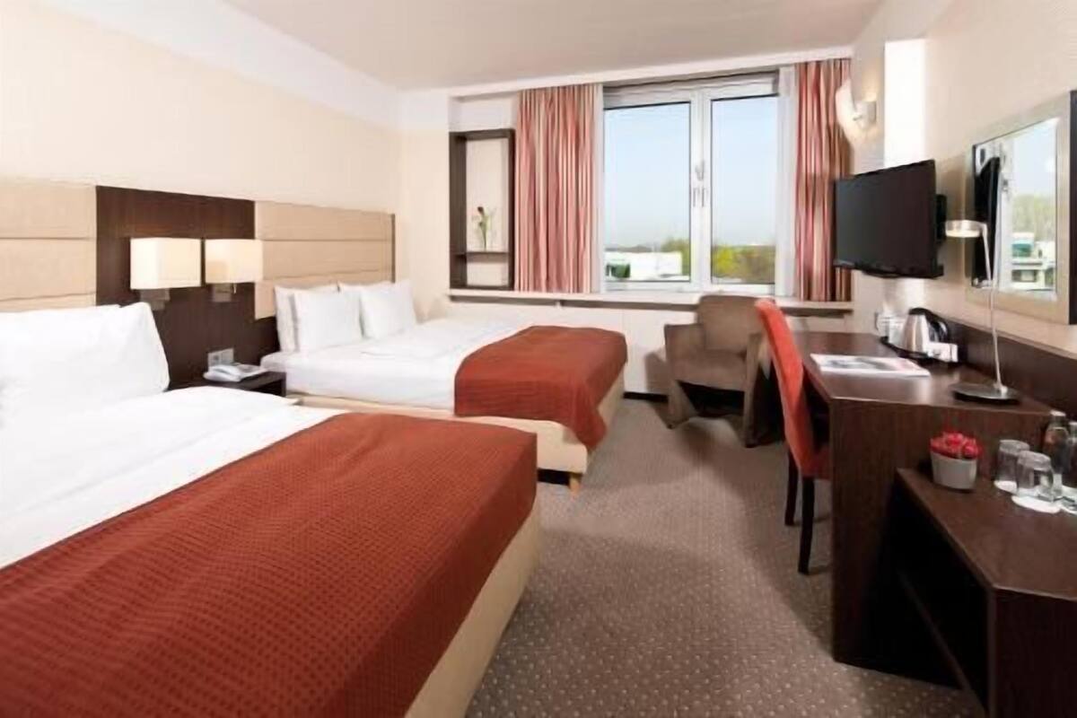 A hotel room with two beds, a desk, a chair, a TV, and a window with curtains.