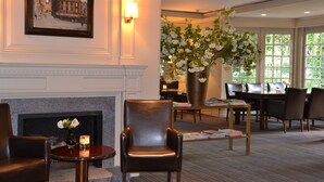 A hotel lobby with a fireplace, seating area, dining table, and large windows.