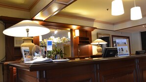 A reception desk with a wooden finish, a large white lamp, and a framed picture on the wall.