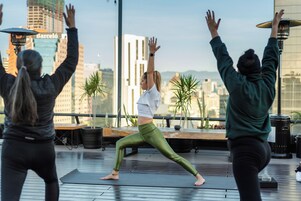 Tres personas practicando yoga en una azotea con vista a la ciudad.
