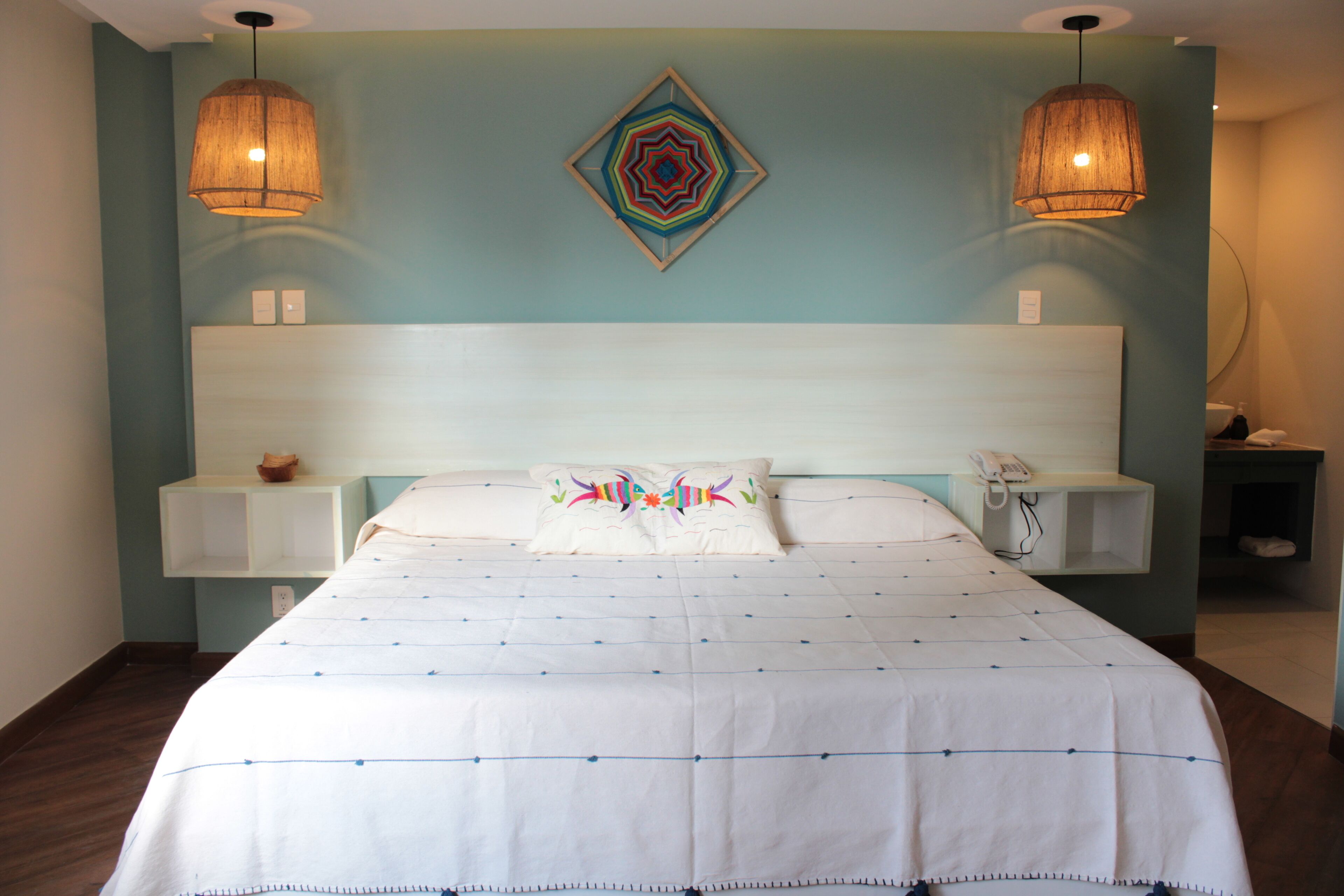 Una cama bien hecha con edredón blanco y detalles azules, un cabecero de madera y dos lámparas de noche.