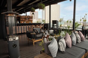 Un bar en la azotea con asientos y zona de bar, con vistas a un paisaje urbano.