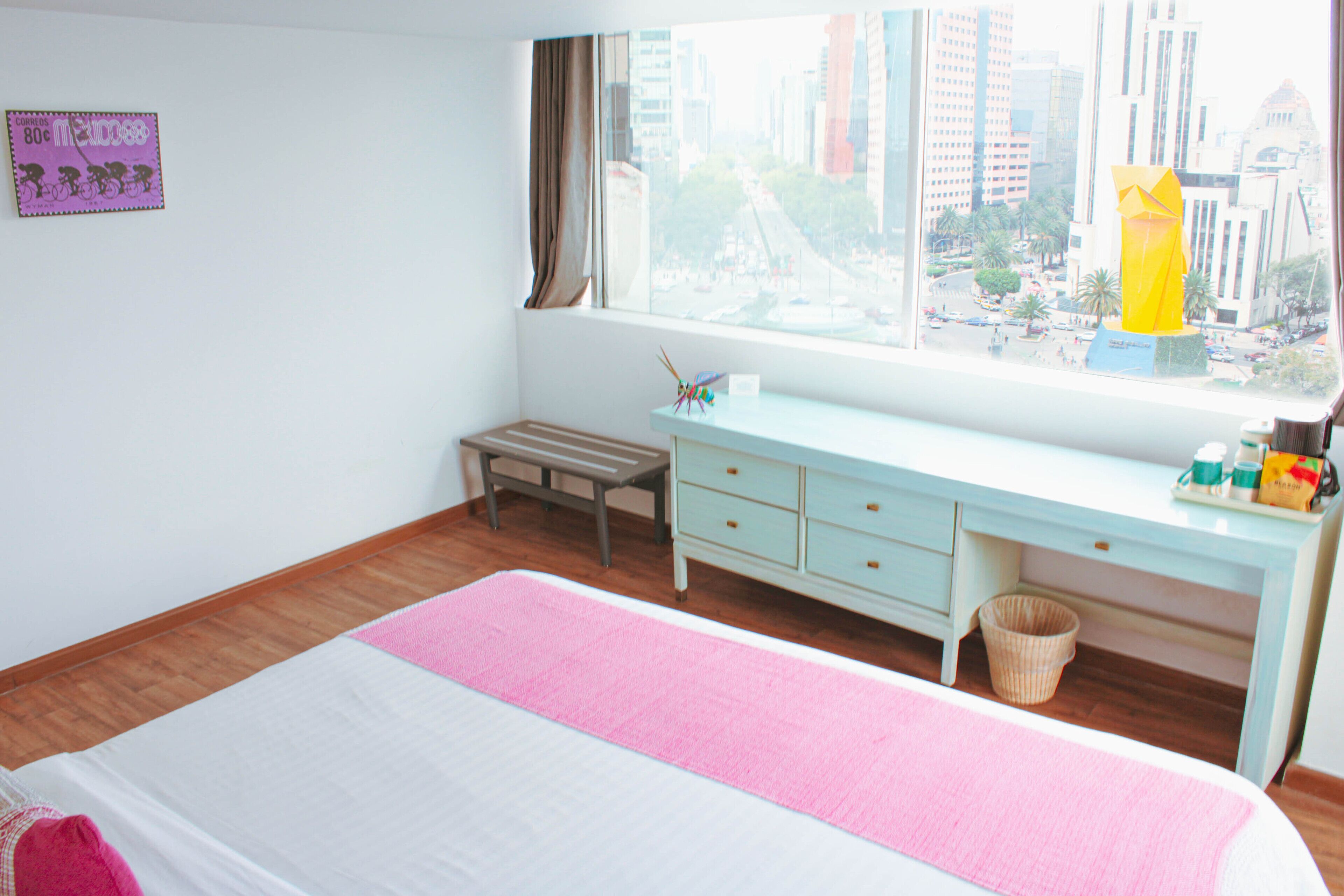 Un dormitorio con cama, escritorio, ventana con vista a la ciudad y un pequeño banco.