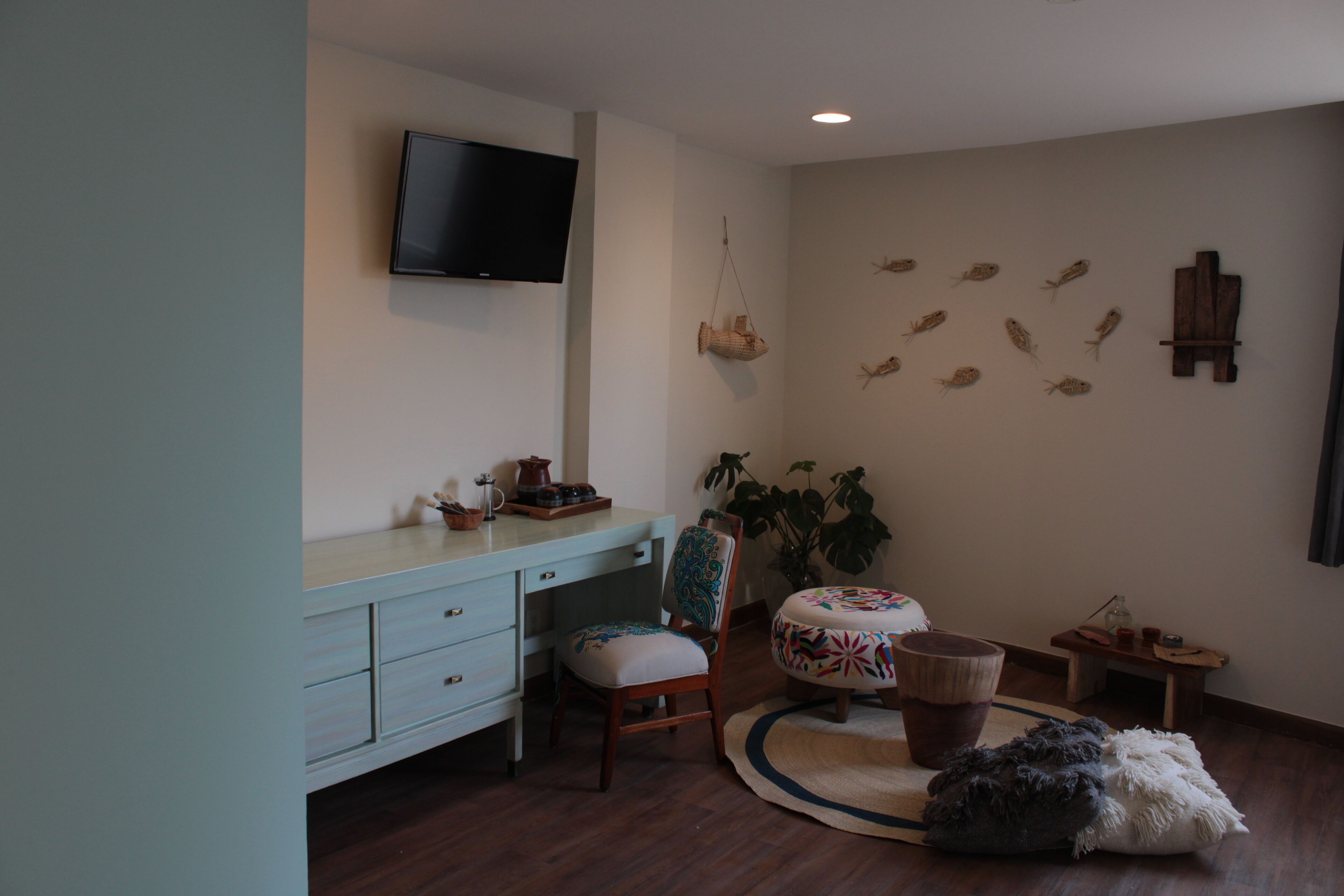 A room with a desk, chair, television, decorative fish wall art, and a round table with a colorful table runner.