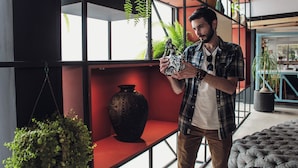 A man holding a decorative item in a modern interior with shelves, a large vase, and potted plants. - Hotel Fontan Reforma Centro Histórico (Mexico City)