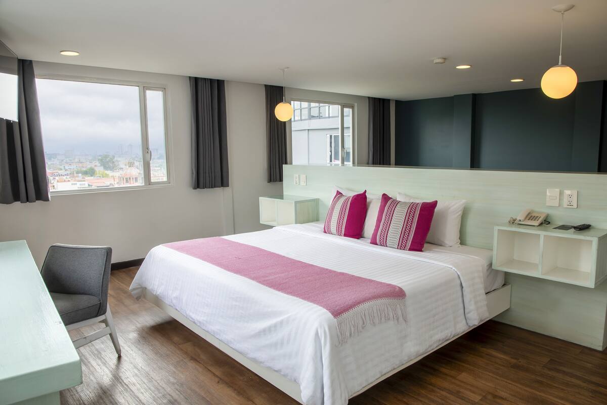 A hotel room with a large bed, a desk, and a view of the city.