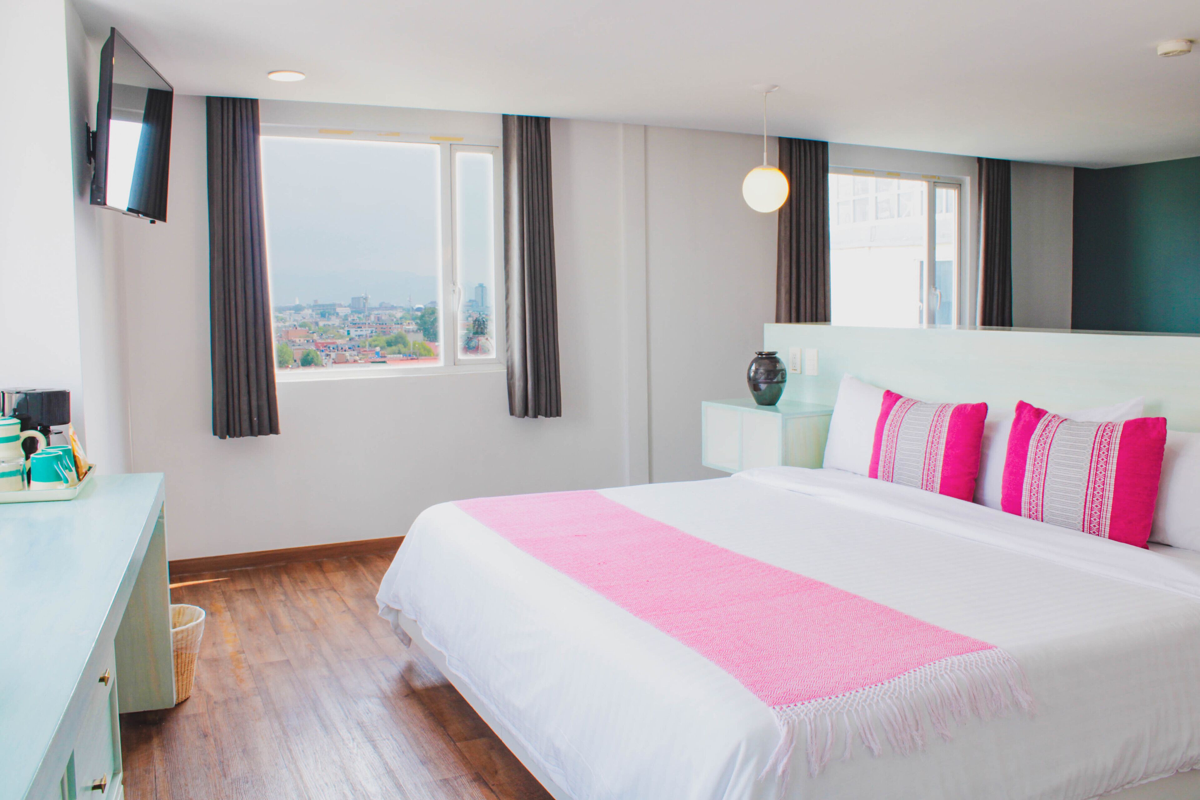 A hotel room with a large bed, a desk, a TV mounted on the wall, and a window with curtains.