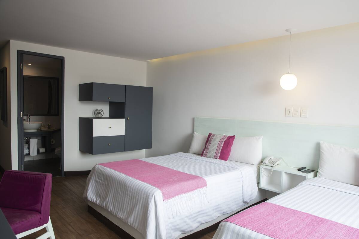 A hotel room with two beds, a wardrobe, a bedside table with a phone, and a bathroom visible through an open door.