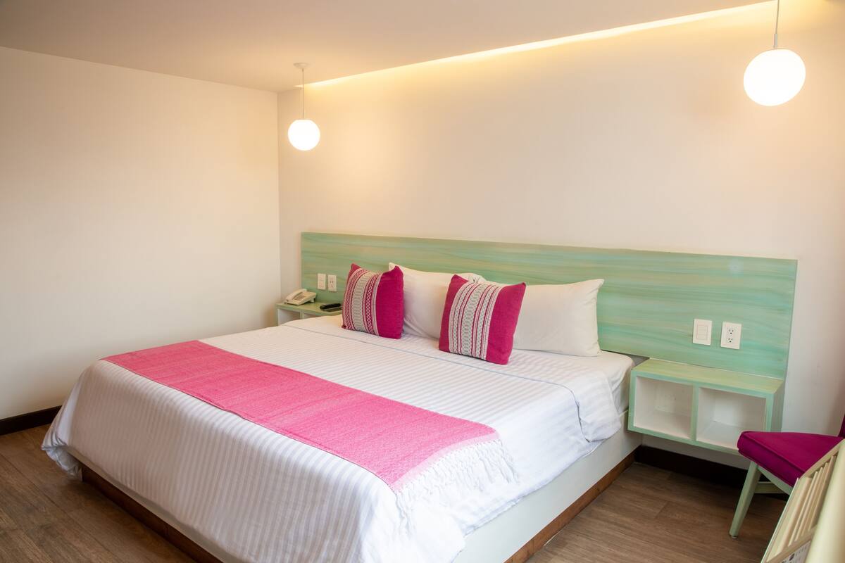 A neatly made bed with a pink blanket, a green headboard, and a bedside table with a phone.
