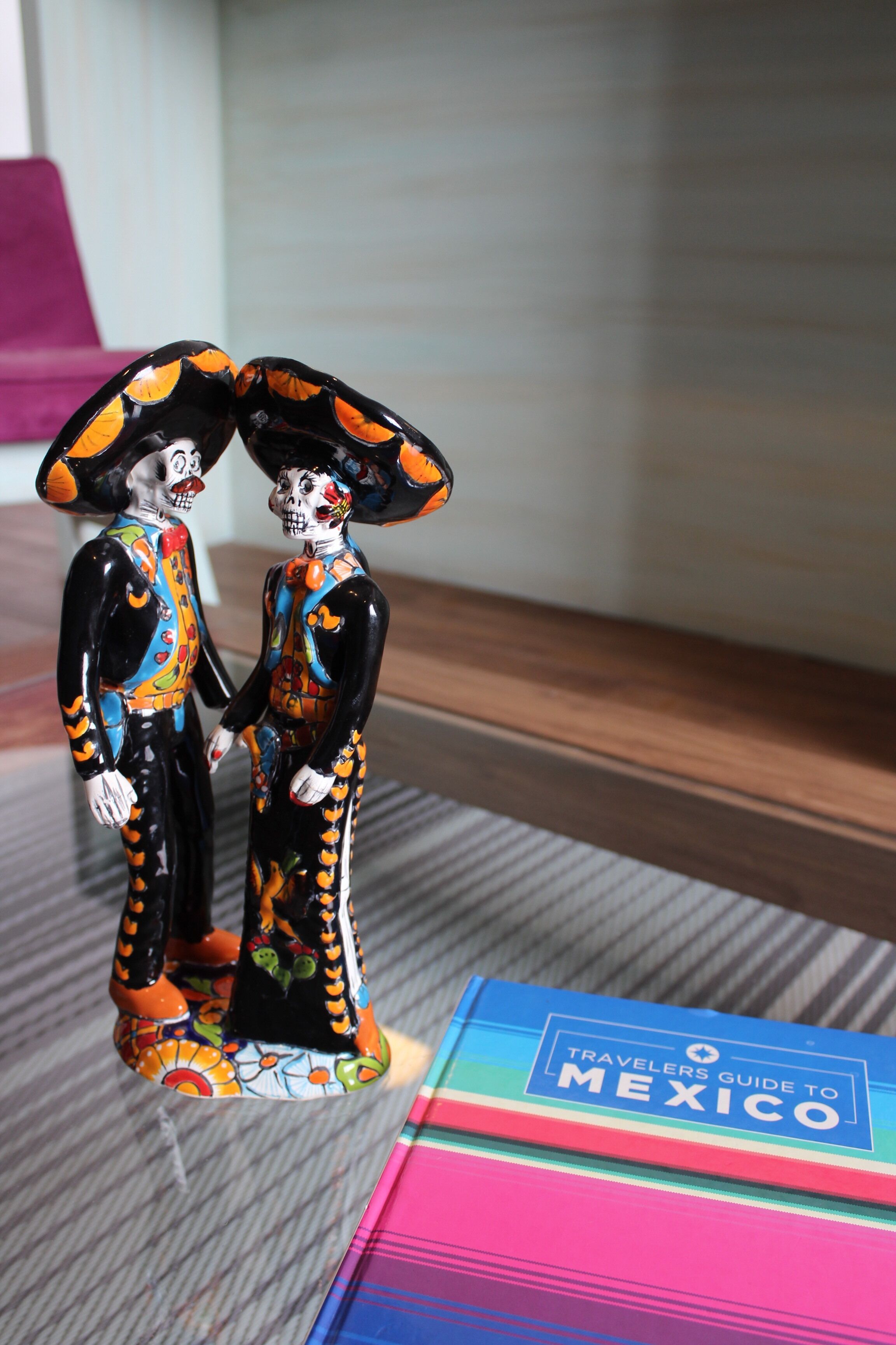 A decorative sugar skull figurine and a guidebook titled "Travelers Guide to Mexico" on a table.
