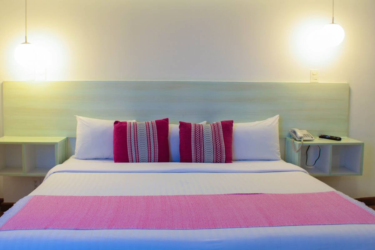 A hotel room with a large bed, two bedside tables, a telephone, and a remote control.