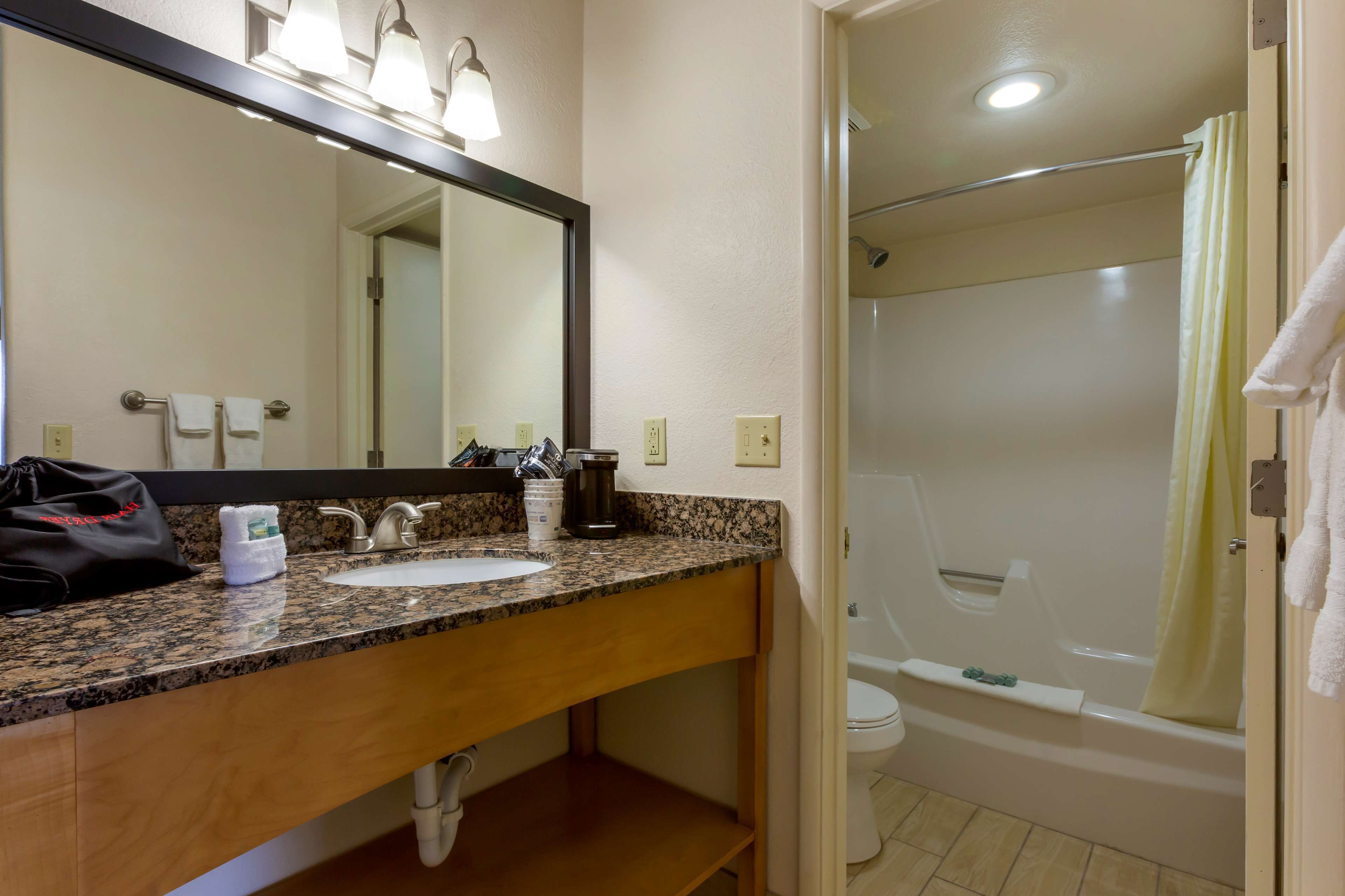 Une salle de bain avec un lavabo doté d’un plan de travail en granit, un miroir, un porte-serviettes, un rideau de douche et une baignoire.