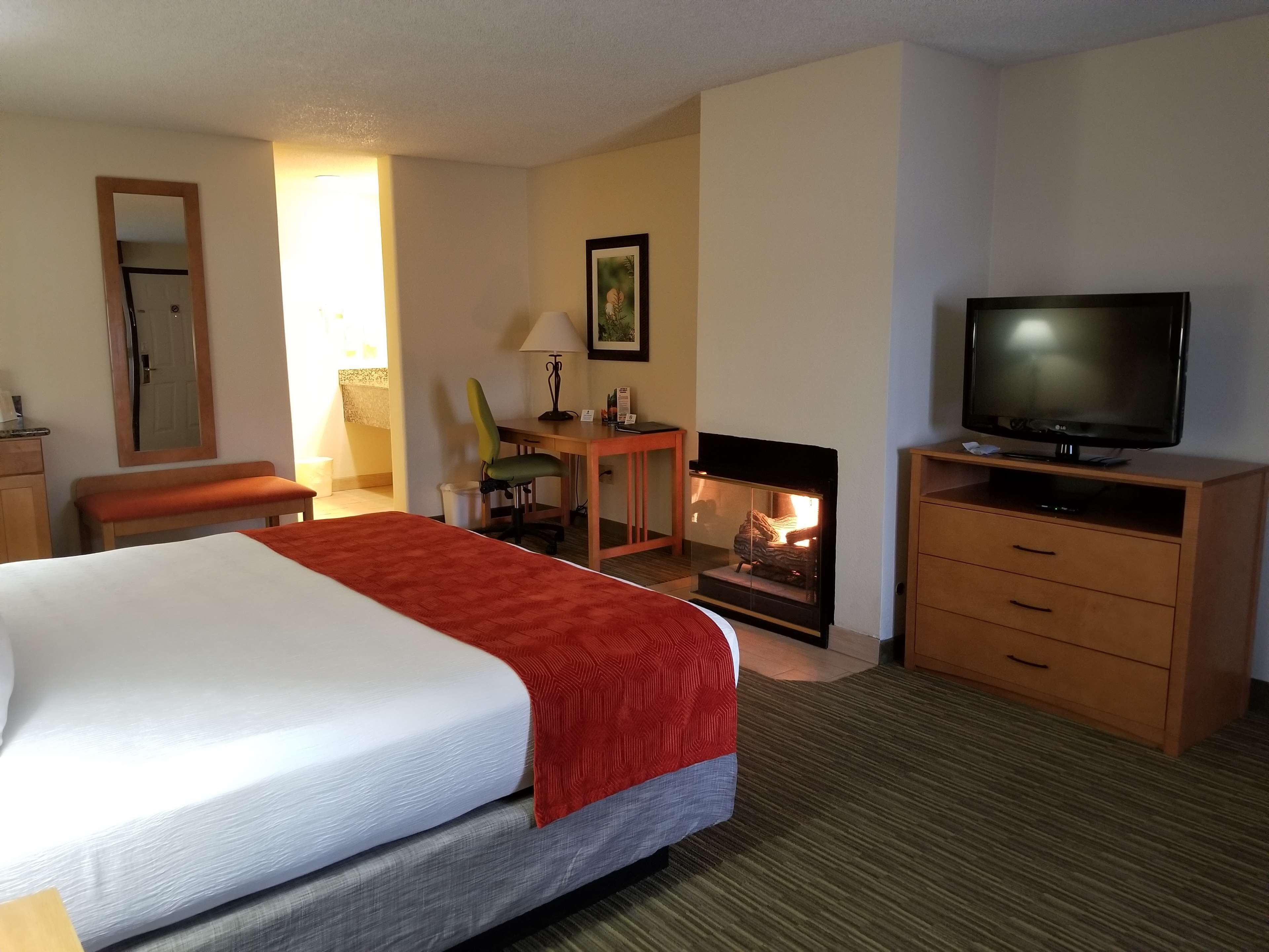A hotel room with a bed, a television, a desk with a chair, a fireplace, and a mirror.