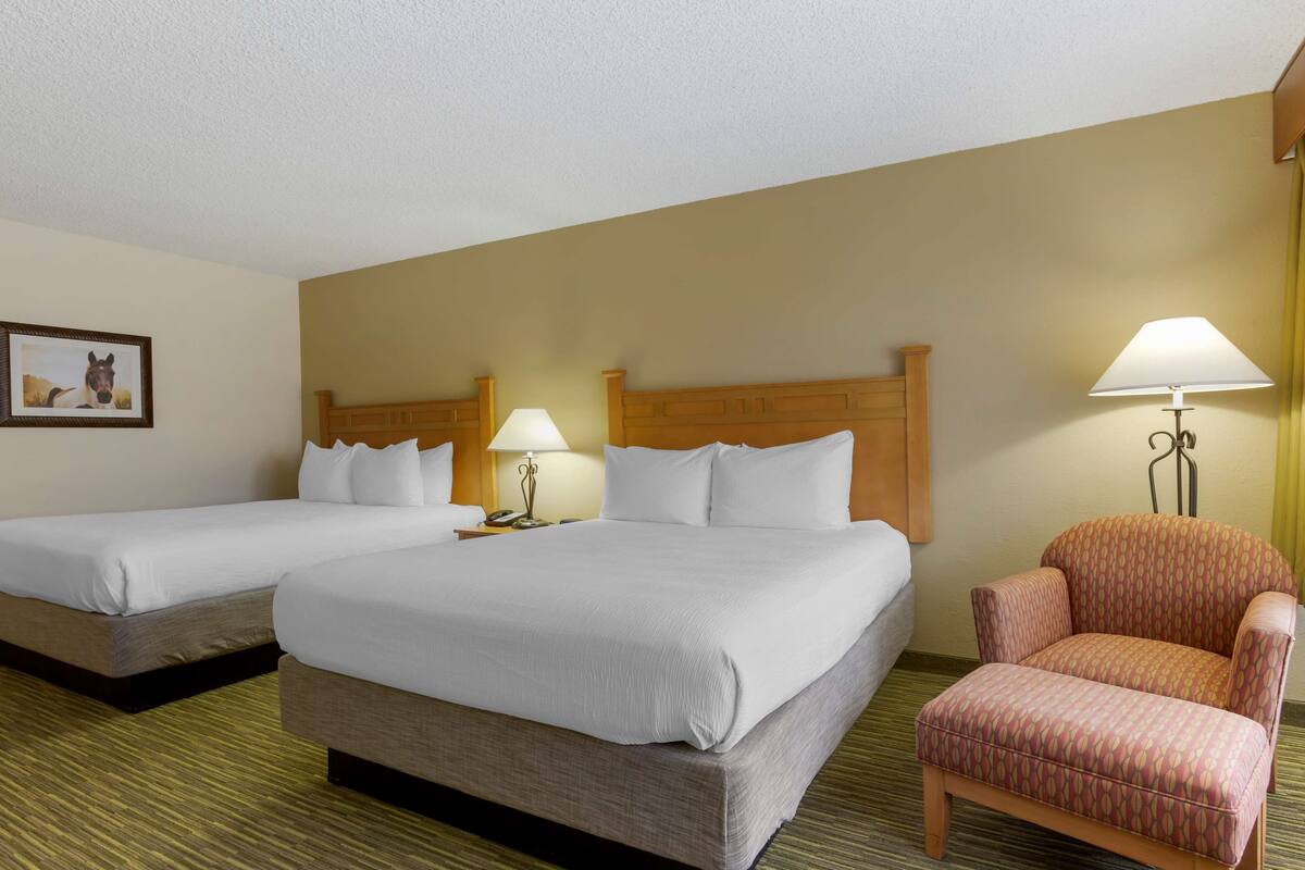 A hotel room with two beds, a chair, and a lamp.