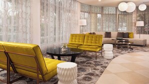 A modern living room with a yellow sofa, a round coffee table, and a beige sofa. There are two lamps and a white side table. - Courtyard Miami in Coral Gables by Marriott (Coral Gables)