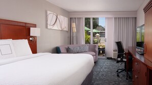 A hotel room with a large bed, a sofa, a desk with a chair, and a television. - Courtyard Miami in Coral Gables by Marriott (Coral Gables)