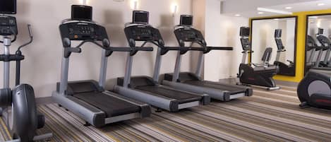 Un gimnasio con cintas de correr, un espejo grande y una alfombra estampada.
