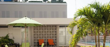 An outdoor seating area with a table and chairs, a green umbrella, and a pool in the background.