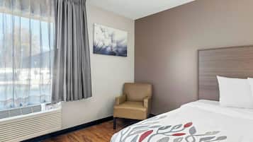 A hotel room with a bed, a chair, a window with curtains, a wall-mounted picture, and a radiator.
