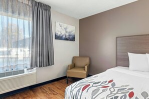 Ein Hotelzimmer mit einem Bett, einem Sessel, einem Fenster mit Vorhängen, einem Wandbild und einer Heizung.