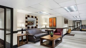 A hotel lobby with a grey sofa, a red armchair, a wooden coffee table, and a small table with a lamp. - Red Roof Inn Charlotte - University (Charlotte)