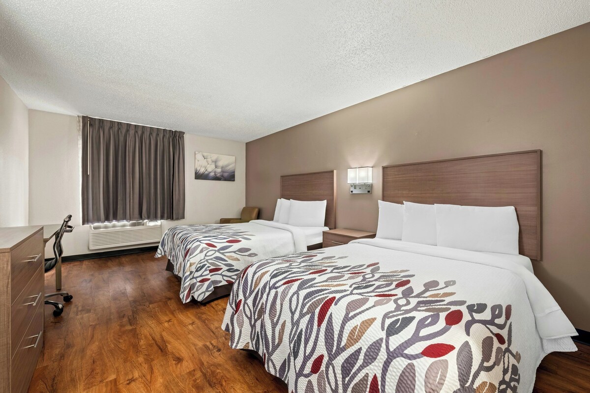 A hotel room with two beds, a desk, a chair, and a window with curtains.