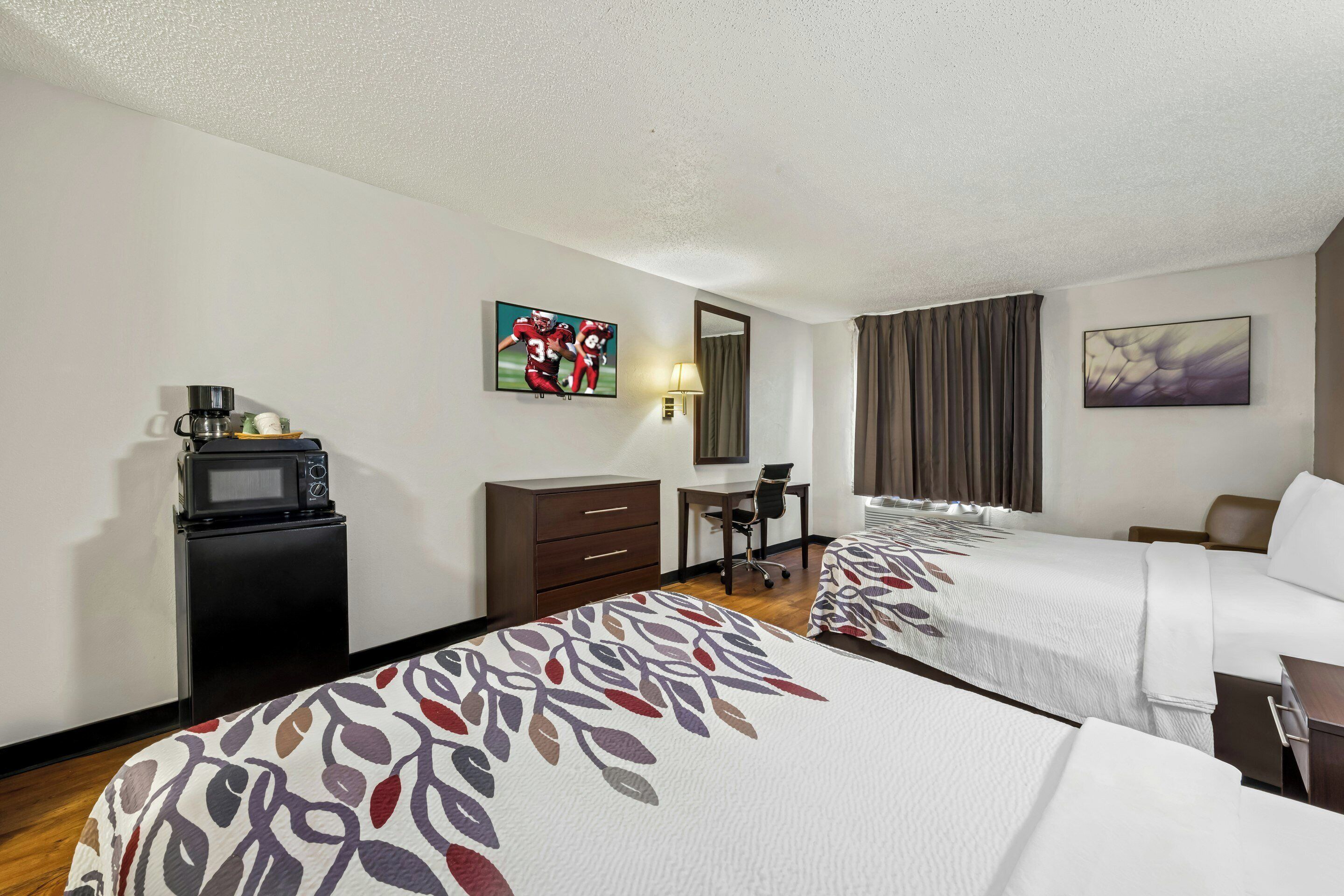 A hotel room with two beds, a desk, a chair, a television, and a coffee maker.